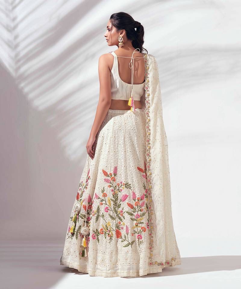 Woman wearing a floral embroidered lehenga with a plain background