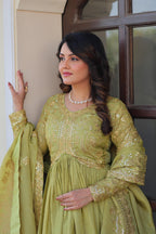 Woman in a green traditional outfit with gold embroidery standing indoors.