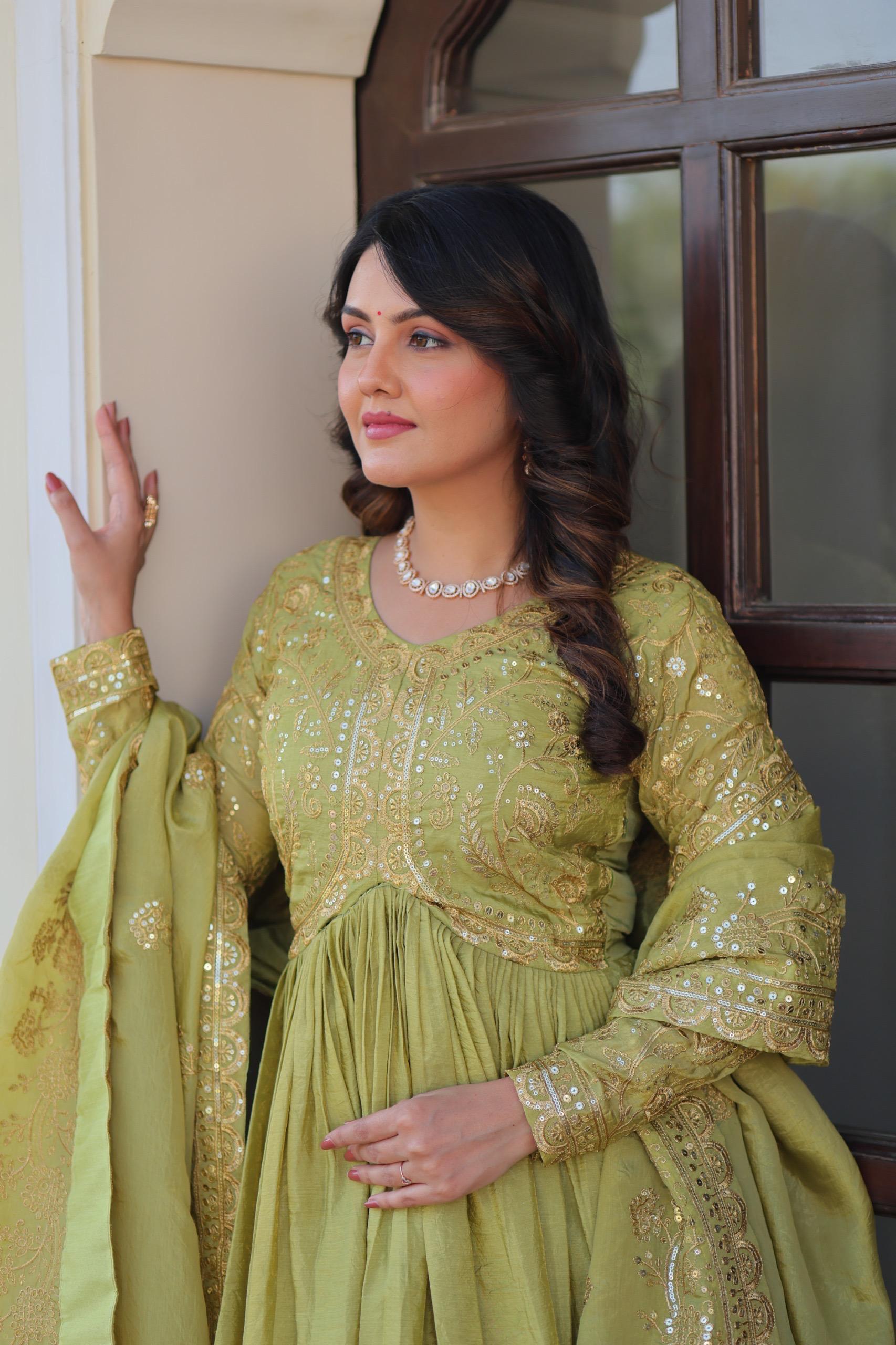 Woman in a green traditional outfit with gold embroidery standing indoors.