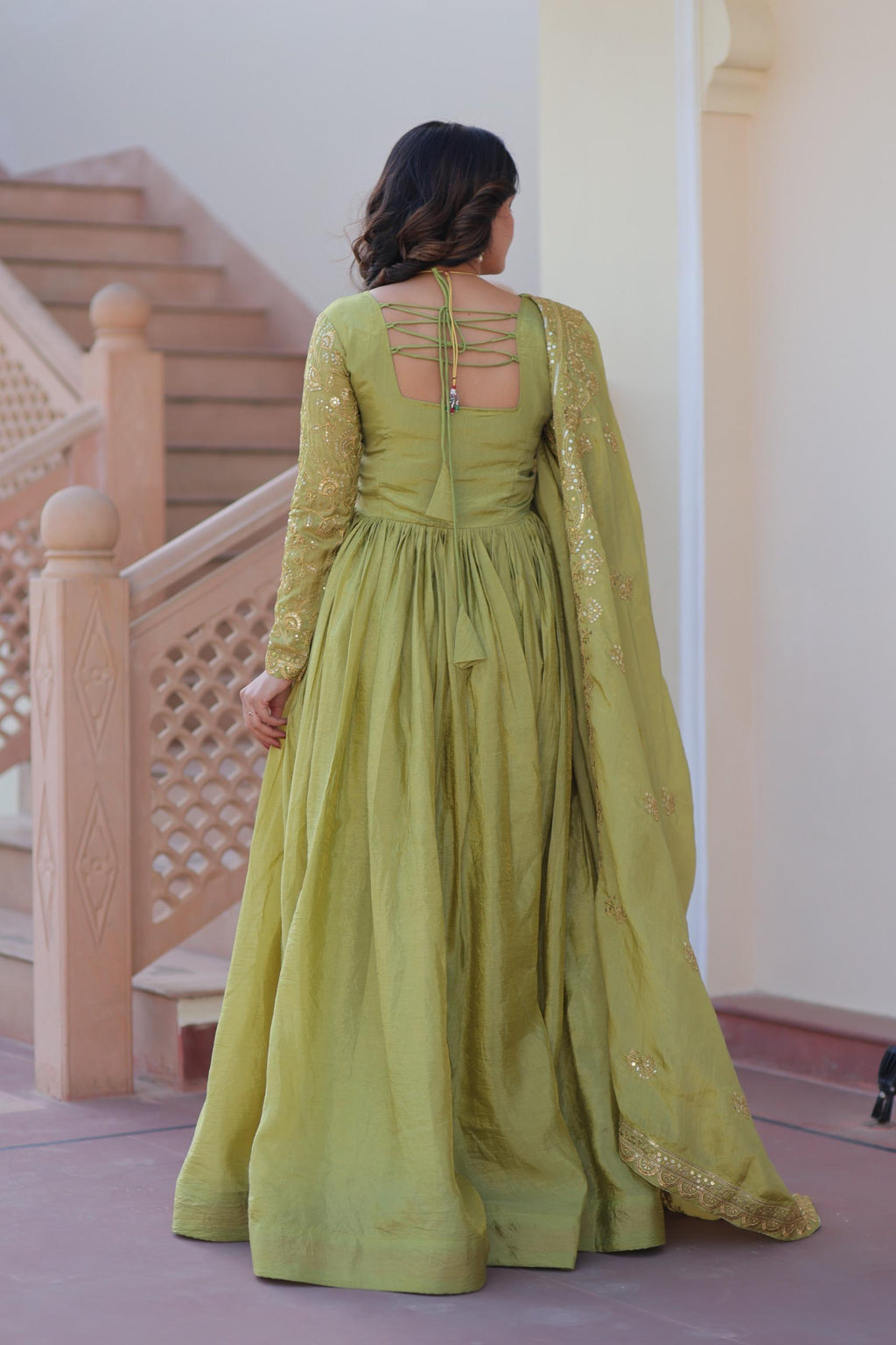 Woman wearing a green dress with intricate detailing in an indoor setting.