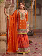 Woman in traditional orange and green embroidered outfit standing in a decorative setting.
