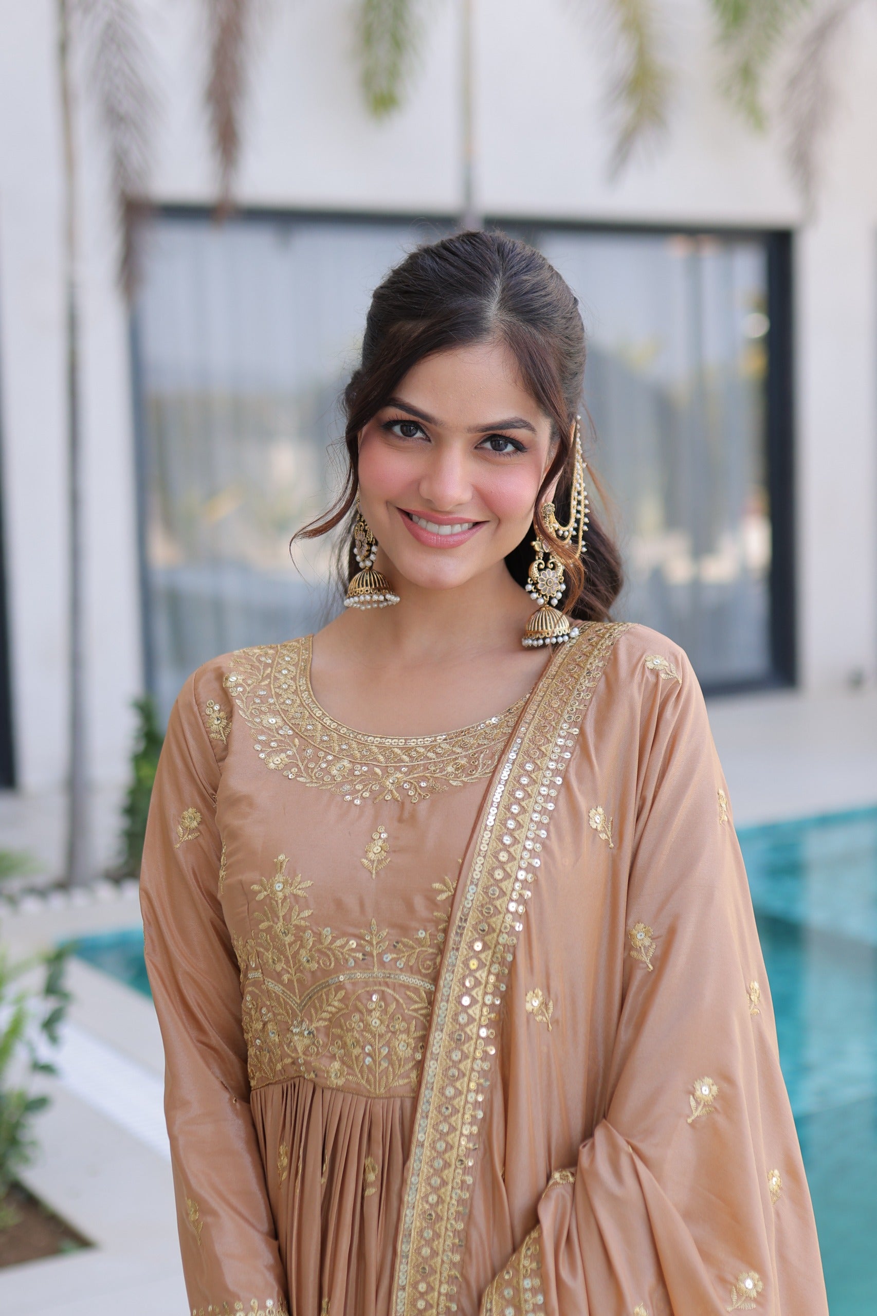 Woman in a beige and gold traditional outfit standing by a pool.