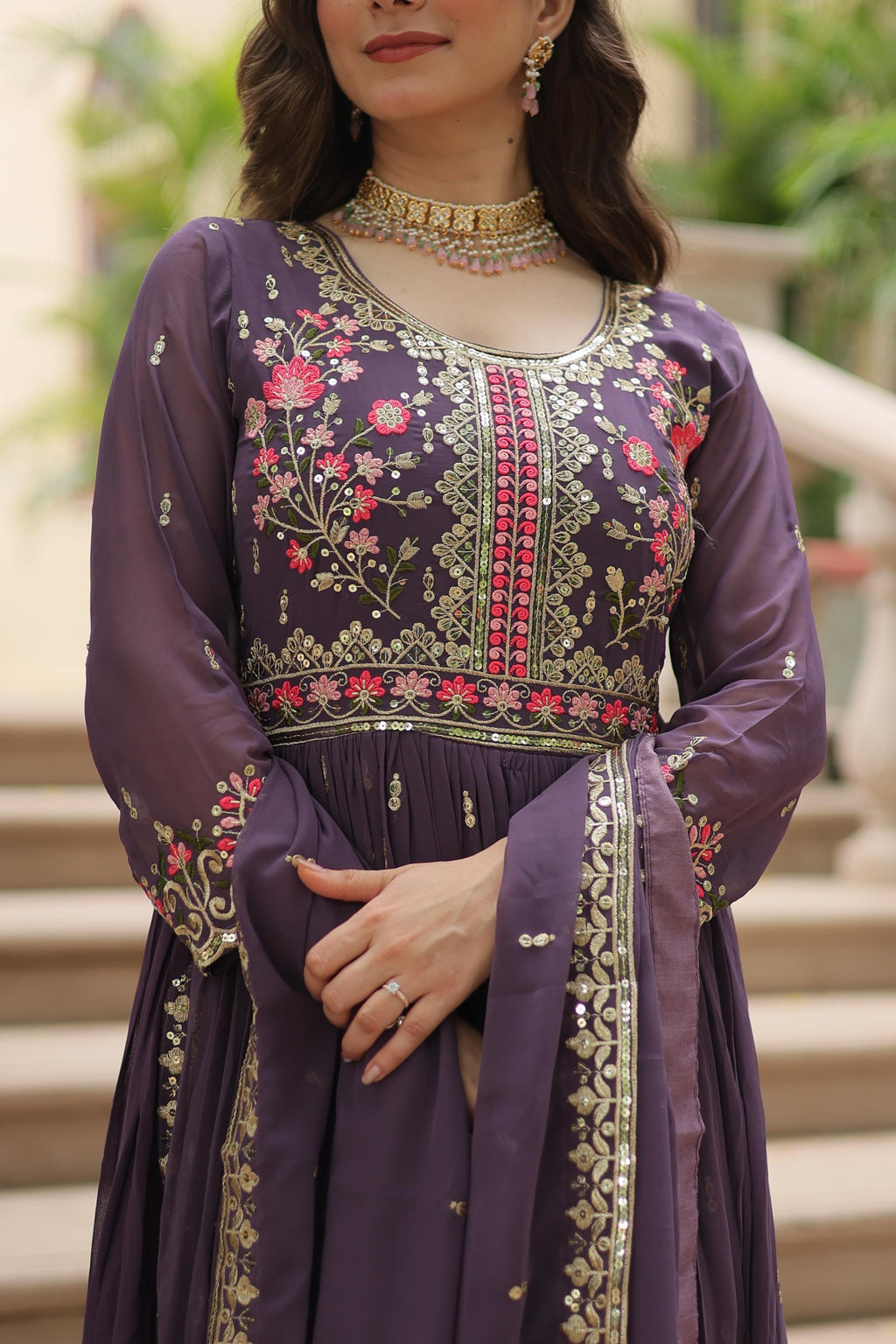 Woman wearing a purple embroidered traditional outfit with a blurred outdoor background