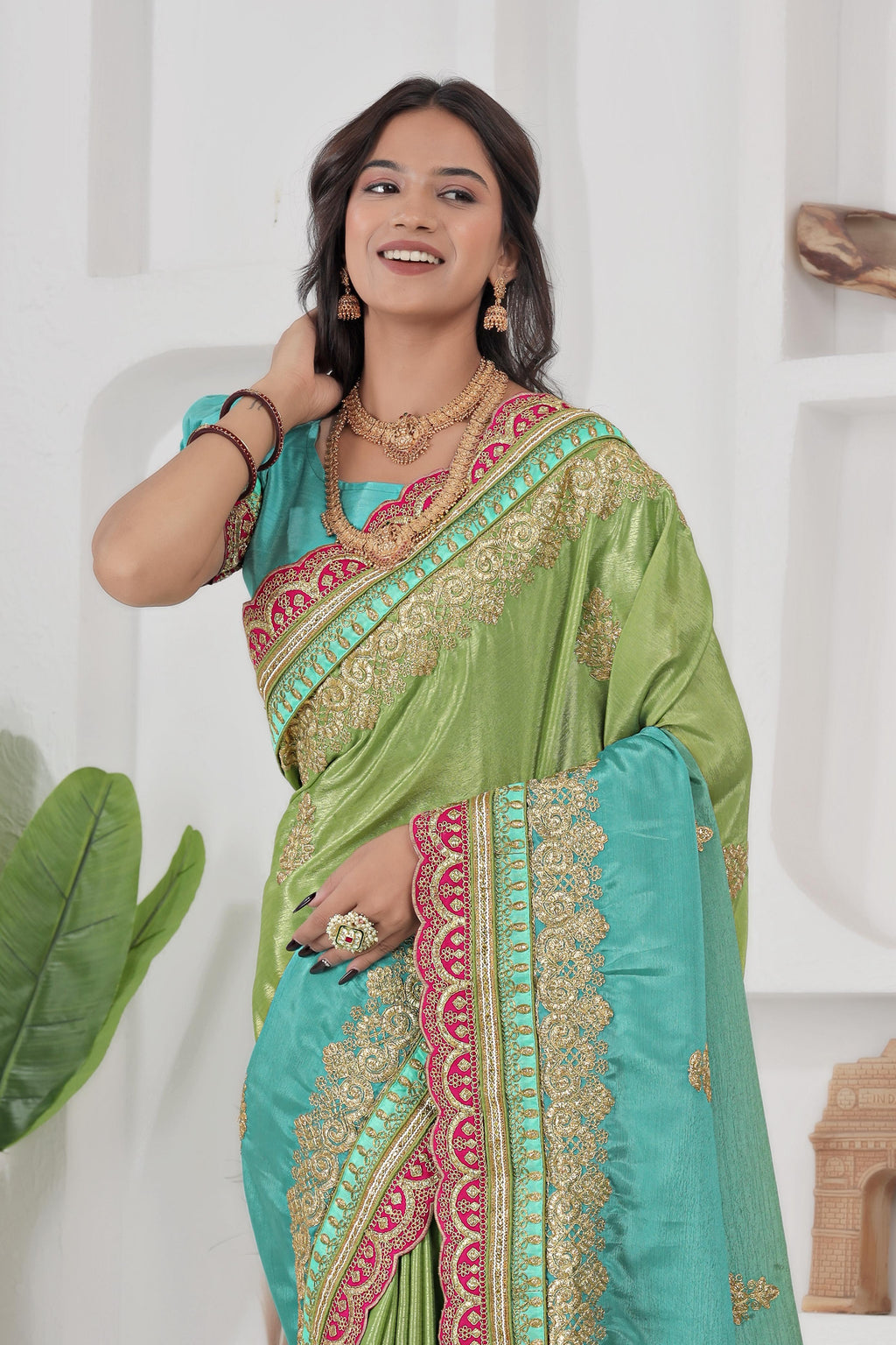 Woman wearing a green and blue saree with intricate patterns, posing against a white background.