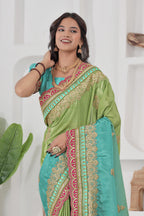 Woman wearing a green and blue saree with intricate patterns, posing against a white background.