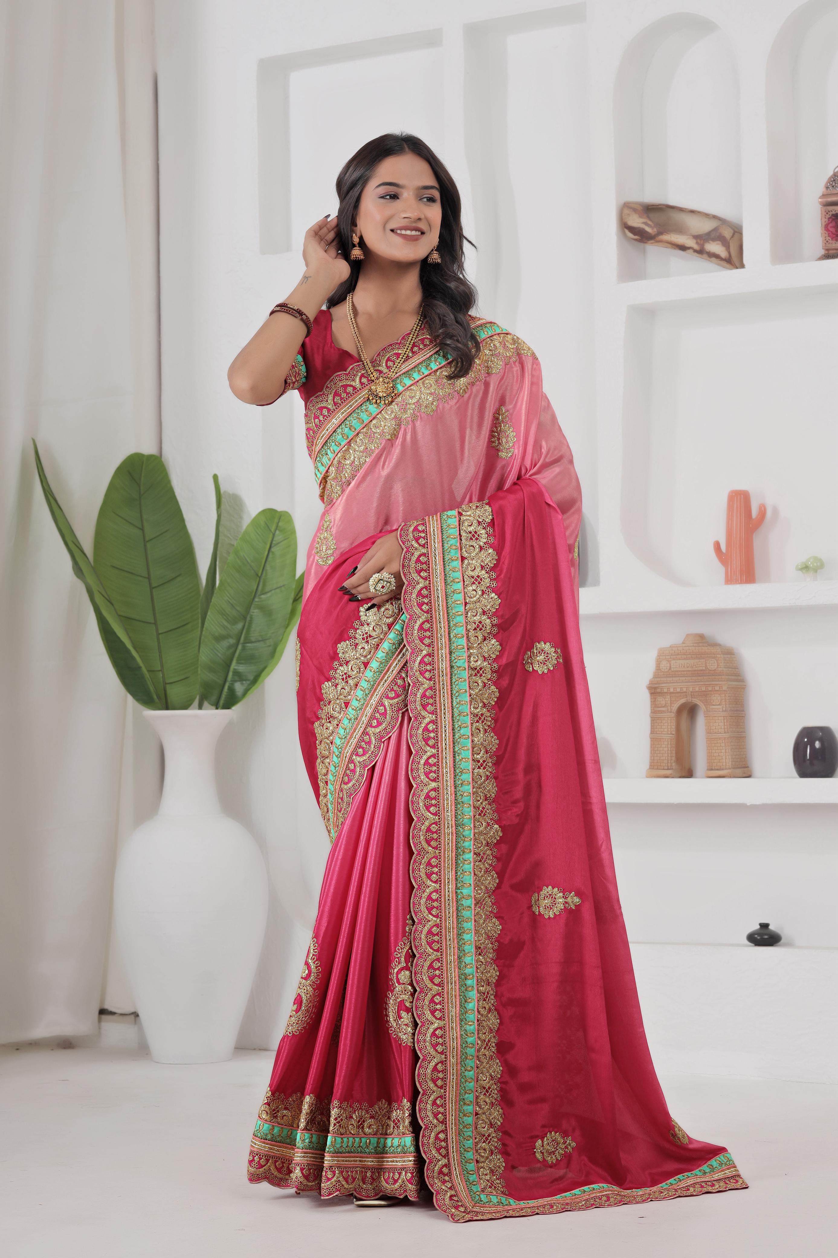 Woman wearing a pink saree with green and gold border in a white room.