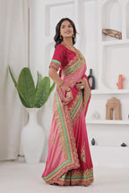 Woman wearing a pink saree with gold and green border in a white room.