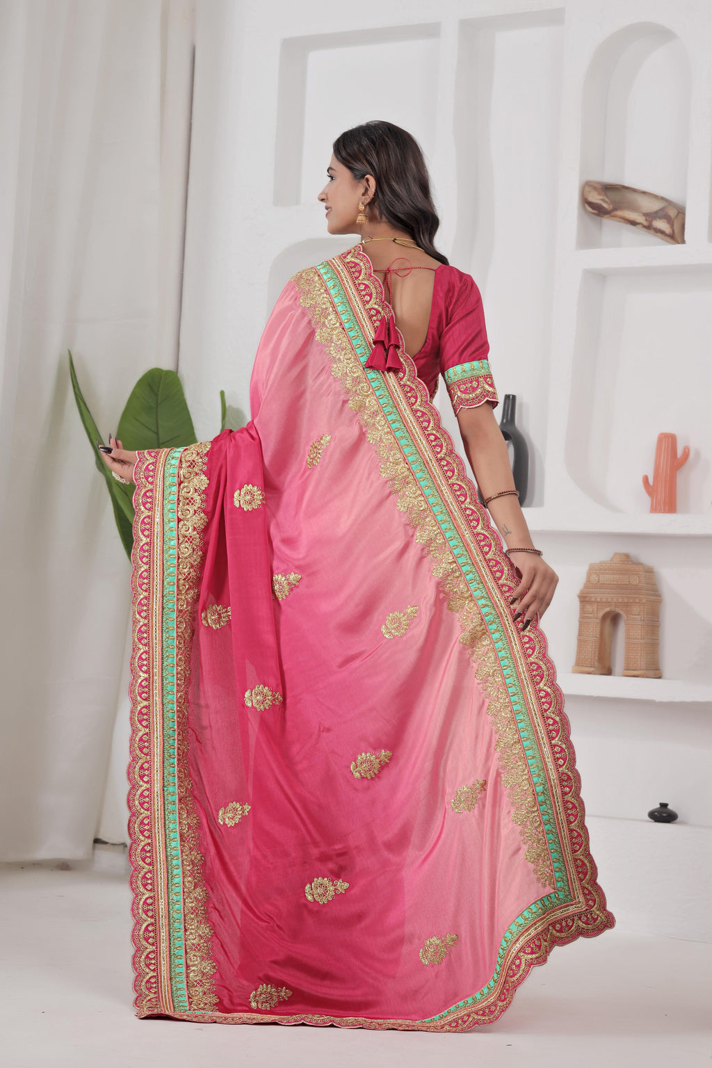 Woman wearing a pink saree with gold and green border indoors.