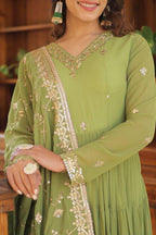 Woman wearing a green embroidered traditional outfit with a wooden background
