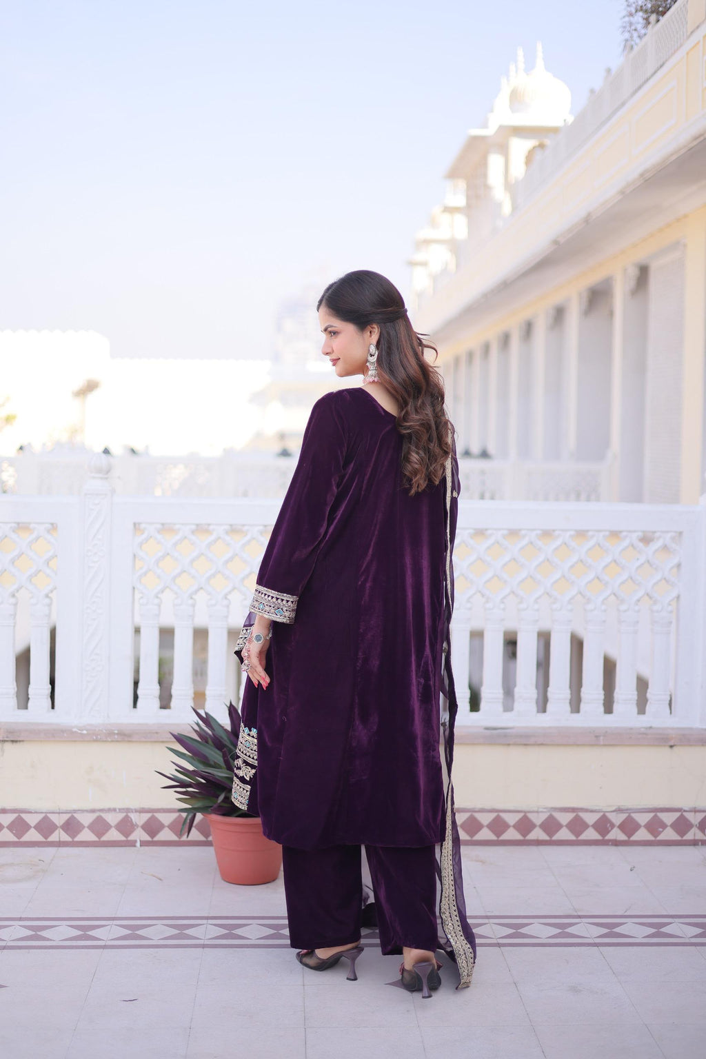Woman in a purple outfit standing on a balcony with white railings and a clear sky.