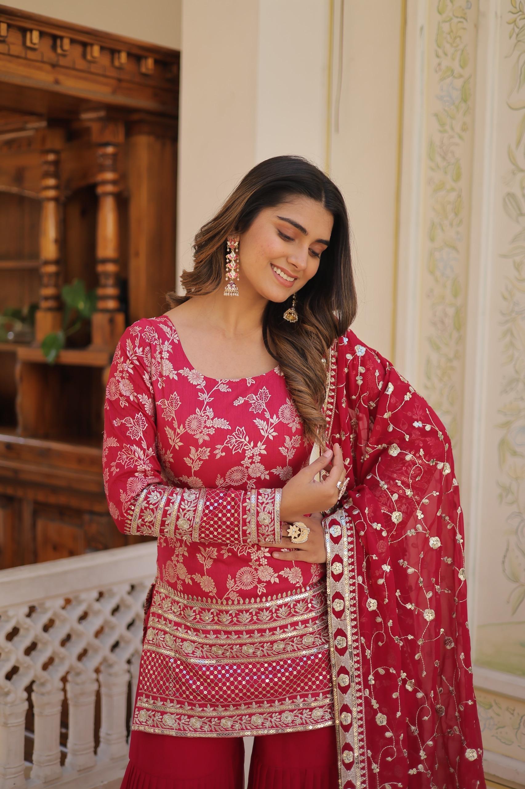 Woman in a traditional pink and red embroidered outfit standing indoors.