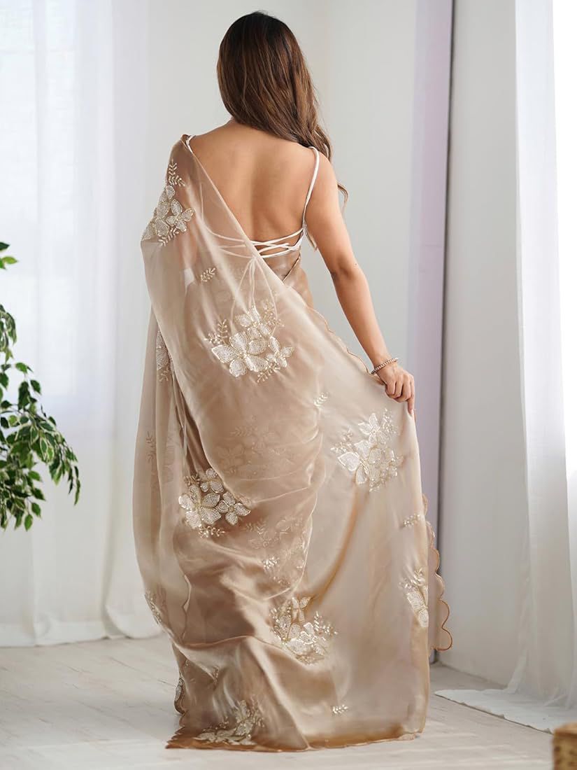 Woman wearing a beige evening gown with floral embroidery in a room with white curtains.