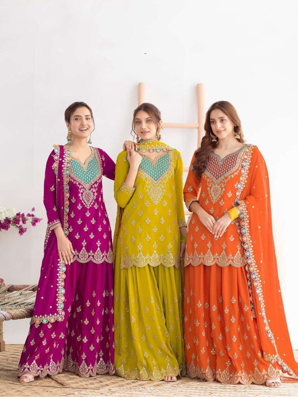 Three women wearing colorful traditional outfits with intricate designs on a white background.