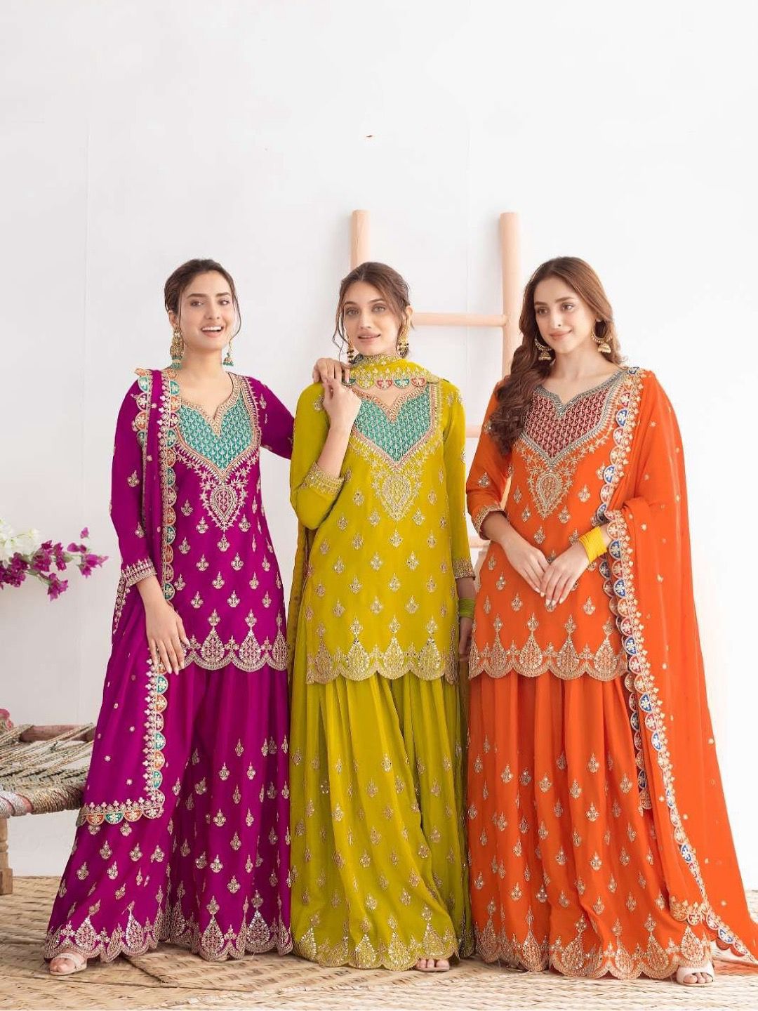 Three women wearing colorful traditional outfits with intricate designs on a white background.
