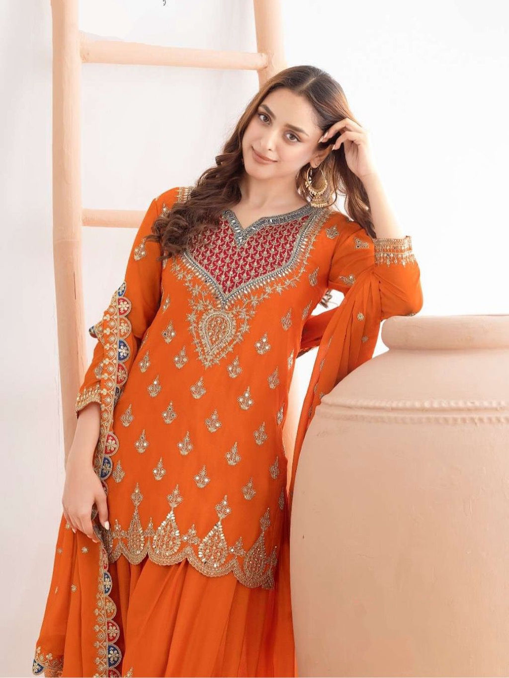 Woman wearing an orange embroidered traditional outfit against a white background