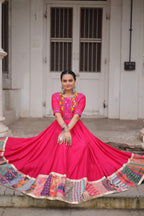 Woman in a bright pink traditional outfit with colorful patterns standing in front of a white door.