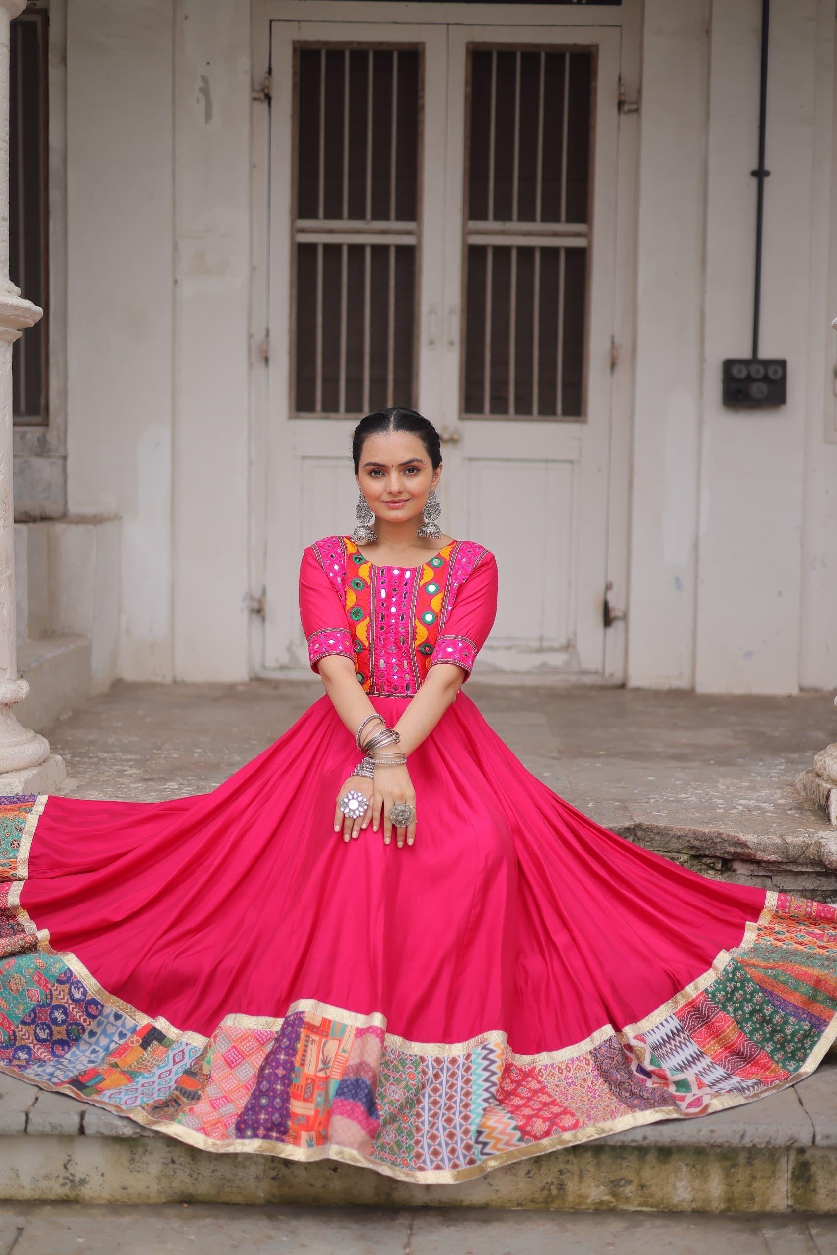 Woman in a bright pink traditional outfit with colorful patterns standing in front of a white door.
