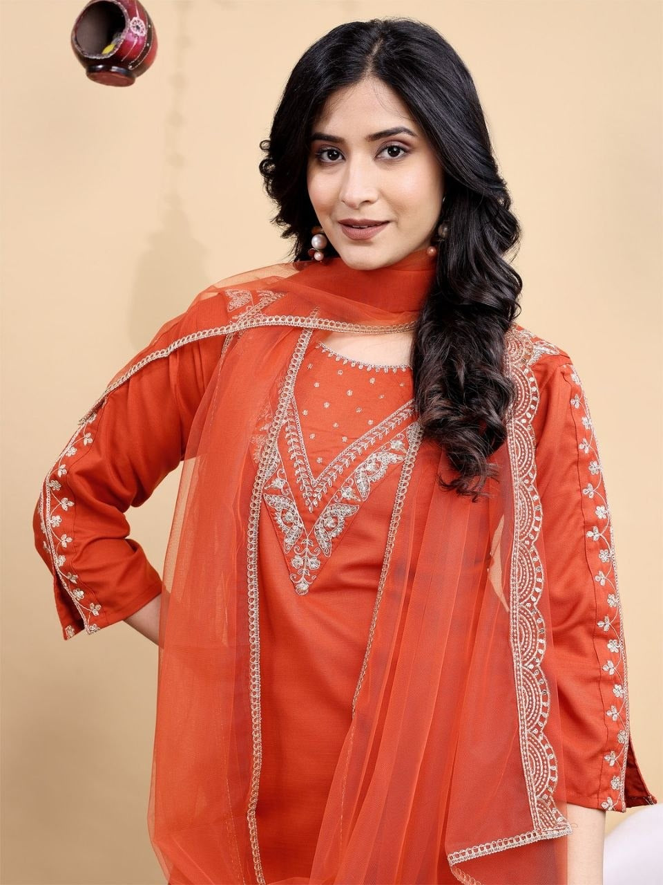 Woman wearing an orange embroidered traditional outfit on a beige background