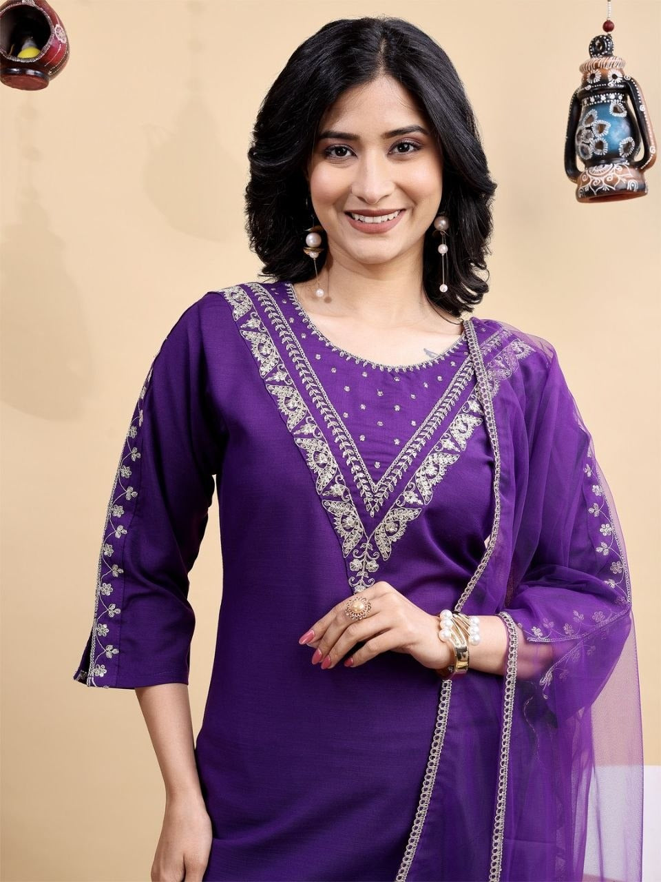 Woman wearing a purple traditional outfit with intricate designs on a beige background