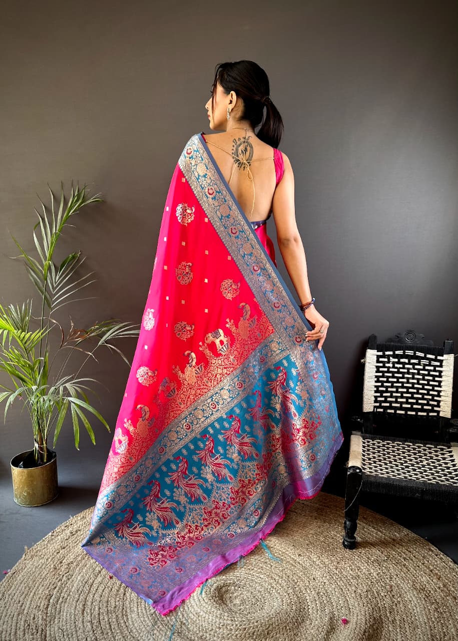 Woman wearing a vibrant saree with a red and blue pattern, standing in a room with a plant and chair.