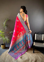 Woman wearing a vibrant saree with a red and blue pattern, standing in a room with a plant and chair.